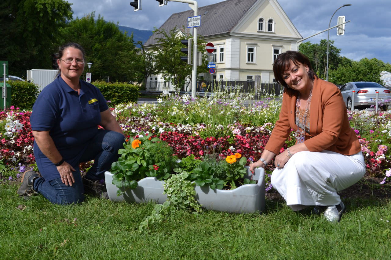 Vizebürgermeisterin Dr.in Oberrauner mit Stadtgarten-Mitarbeiterin Corinna Spasojevic im Stadtpark vor einem Blumen-Ensemble und einem Exemplar der beim CCV verwendeten Kräuterkistln.