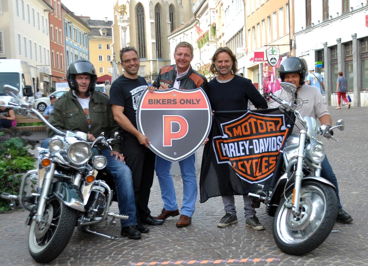 Tourismusverband-Obmann Dr. Martin Domenig, Bürgermeister Günther Albel und Hubert Marko, stellvertretender Aufsichtsratsvorsitzender des Stadtmarketings mit Harley-Gästen auf dem Villacher Hauptplatz.
