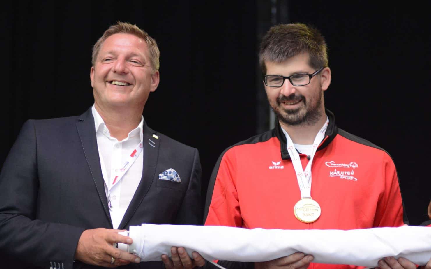 Villachs Bürgermeister Günther Albel und Mario Horn von der Diakonie de la Tour Treffen mit der eingerollten und übergebenen Special Olympics Fahne